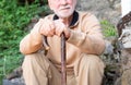 Pensive old senior man in winter sweater outdoors of a rural house leaning on walking stick. Caucasian man with beard and white Royalty Free Stock Photo