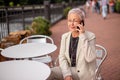 Pensive pleasant woman with phone sitting at the table in the outdoor cafe