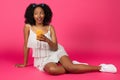 Pensive positive millennial african american woman in dress and sneakers sit on floor, chatting on smartphone Royalty Free Stock Photo