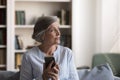 Pensive positive senior smartphone user woman sitting on home couch