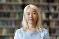 Pensive pretty Asian blonde student girl posing in university library