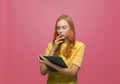 Pensive puzzled young girl looking at tablet, solving problem, thinking out idea, making choice on pink background Royalty Free Stock Photo