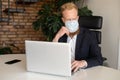 Pensive red-haired businessman in smart casual suit wearing protective face mask