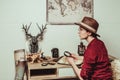 pensive retro style woman in hat with magnifying glass sitting at table