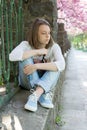 Pensive and sad girl sitting near the fence on the background of blooming