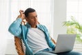 Pensive sad young african american man typing on computer in light living room interior Royalty Free Stock Photo