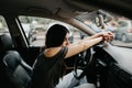 Pensive and sad young woman with arms on the steering wheel of the car on a rainy day