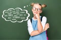 pensive schoolchild in glasses looking up near blackboard with different professions