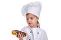 Pensive serious chef girl in a cap cook uniform, appraising the eclair. Looking at it ready to eat. Landscape image Royalty Free Stock Photo