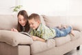 Pensive siblings reading book lying on sofa Royalty Free Stock Photo