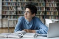 Pensive student guy staring aside, sit at table in library Royalty Free Stock Photo