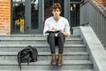 Pensive student sitting on modern building steps and making notes in notepad. Royalty Free Stock Photo