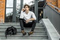 Pensive student sitting on modern building steps and making notes in notepad. Royalty Free Stock Photo