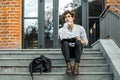 Pensive student sitting on modern building steps and making notes in notepad Royalty Free Stock Photo