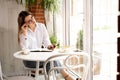 A pensive stylish girl in a cafe is dreaming while sitting by the window looking for new ideas. Young woman with glasses Royalty Free Stock Photo