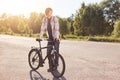 Pensive teenage boy standing on road, keeping hand on handle bar of his bike, waiting for others cyclists to have journey together Royalty Free Stock Photo