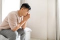 Pensive thoughtful mature asian man wearing pajamas sitting on bed