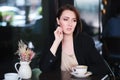 Pensive or thoughtful woman sitting at table in cafe wearing black jacket