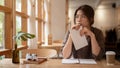 A pensive, thoughtful young Asian woman sits at a table in a beautiful, cosy coffee shop