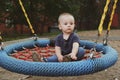 Pensive one year old baby boy swings on a swing. Royalty Free Stock Photo