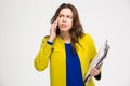 Pensive unpleased young woman with clipboad talking on mobile phone Royalty Free Stock Photo