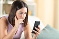 Pensive woman checking smart phone content at home Royalty Free Stock Photo