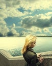 Pensive woman leaning on granite sea-wall ander sky with clouds