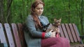 Pensive woman sits on a bench in the woods and irones two small dogs on her knees.