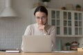 Pensive woman wear glasses use laptop seated in kitchen Royalty Free Stock Photo