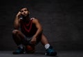 Pensive young African-American basketball player in sportswear sitting on a ball over dark background. Royalty Free Stock Photo