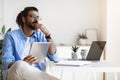 Pensive Young Arab Male Freelancer Using Gigital Tablet And Daydreaming At Home