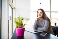 Pensive young beautiful businesswoman working on laptop and keeping hand on chin while sitting at her working place Royalty Free Stock Photo