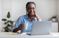 Pensive young black female freelancer drinking coffee at workplace in home office