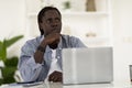 Pensive Young Black Man Sitting On Desk With Laptop And Looking Away Royalty Free Stock Photo