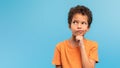 Thoughtful boy in orange, pondering on blue background, free space Royalty Free Stock Photo