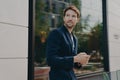 Businessman in dark suit holding smartphone and looking aside while walking city street Royalty Free Stock Photo