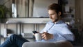 Pensive young businessman focused on smartphone holding cup of tea