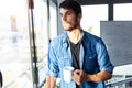 Pensive young businessman looking through the window while drinking coffee and taking a break in the office Royalty Free Stock Photo