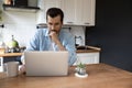 Pensive young man work on laptop in kitchen thinking Royalty Free Stock Photo