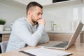 Pensive young Caucasian man sit at table at home kitchen work online on laptop pondering thinking. Thoughtful millennial Royalty Free Stock Photo