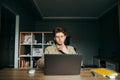 Pensive young developer working at home on a laptop at work against the backdrop of a cozy bedroom, staring intently at the