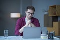 Pensive young German man home office employee sits at desk at workplace operates online on laptop
