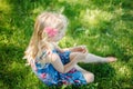 Pensive young girl in blue dress sitting on ground outdoors on summer sunny day. Cute pretty little child kid dreaming thinking on Royalty Free Stock Photo