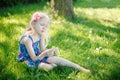 Pensive young girl in blue dress sitting on meadow grass outdoors on summer sunny day. Cute pretty little child kid dreaming Royalty Free Stock Photo