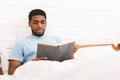 Pensive young guy reading book in bed Royalty Free Stock Photo