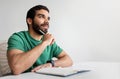 Pensive young man with a beard in a green shirt holding a pen to his chin Royalty Free Stock Photo