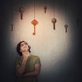 Pensive young man keeps hand under chin, thoughtful gesture, looking up focused, choosing a hanging golden key instead of multiple Royalty Free Stock Photo