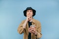 Pensive young man in panama and shirt with a smartphone in his hand stands on a blue background, looks away and thinks Royalty Free Stock Photo