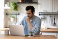Pensive young man work on laptop at home kitchen Royalty Free Stock Photo