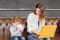 Pensive young mother sitting on sofa with little daughter, using laptop, working distantly at home. Attractive business Royalty Free Stock Photo